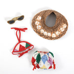 vintage 1950s 4 piece 18 inch doll accessory set including glitter dark lens sunglasses in upper left corner with open top raffia sun hat with white seashells upper right corner and 2 piece bikini red white blue green purple yellow diamond print on bottom area of image all lying on white background