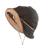 shiny black straw hat with plaited beige brown straw brim partially flipped with black beige grosgrain ribbon trim shown with hat turned to side on thin silver 4 leg metal hat stand against white background