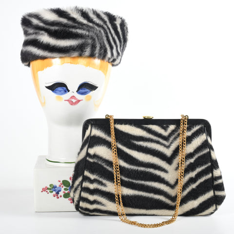 vintage 1960s zebra print pill box faux fur hat shown on ceramic wig holder with painted face left image and matching zebra print faux fur frame hinge purse with gold chain handle draped across front of bag sitting against wig form all on white background