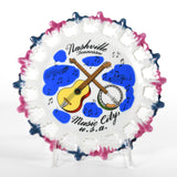 pink and blue iridescent tipped punched out lace edging ceramic Nashville Tennessee plate featuring a guitar, banjo and floating music notes on white ceramic with plate standing on white background