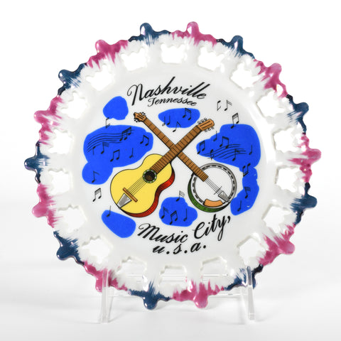 pink and blue iridescent tipped punched out lace edging ceramic Nashville Tennessee plate featuring a guitar, banjo and floating music notes on white ceramic with plate standing on white background