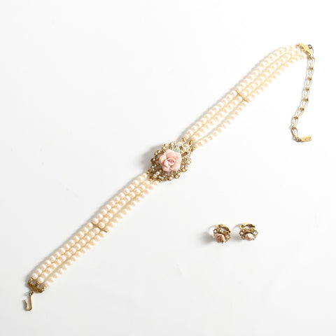 true vintage 1980s 3 strand faux pearl choker with center pendant porcelain pink rose shown angled from bottom left to upper right lying flat with two porcelain rose set on metal clip on earrings on lower right image all on white background