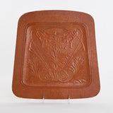 Genuine antique 1900s art nouveau brown pressed fiberboard seat cover panel shown on clear stand all on white background