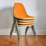 true vintage 1970s orange fabric cream trim zinc finish base 4 stackable eames fiberglass shell chairs shown stacked angled to right on wood floor with white wall and woodwork in natural light