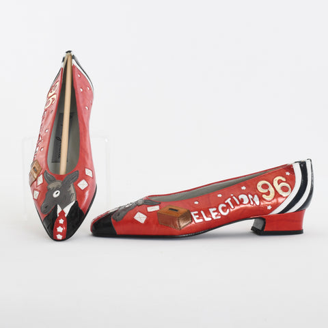 true vintage 1996 novelty election shoes featuring democratic donkey wearing a suit with star tie on toe box with election paper ballots and box on side along with Election 96 and white and blue stripes with red main body shown with right shoe tilted up on left image with left shoe horizontally placed all on white background 