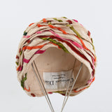 true vintage cream slub silk with various colors of pink, red orange, green, taupe velveteen ribbons woven through the turban folds shown on thin silver metal 4 leg hat stand with Christian Dior label showing at the back of the inner hat all on white background