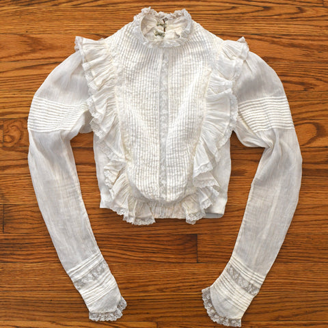 antique 1890s white puff sleeve pin tuck pigeon blouse with lace inserts and edging lying flat on warm brown hardwood floor