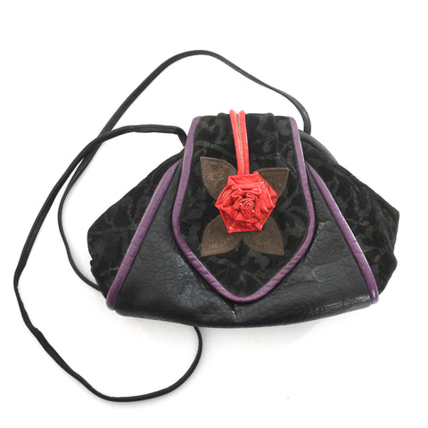 true vintage 1980s black shoulder strap purse piped in eggplant purple with a leather red rosette on top flap shown lying flat white surface