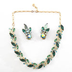 true vintage 1950s emerald green marquis rhinestones offset with smaller lighter green marquis cut rhinestone and smaller round aurora borealis blue rhinestones in a linked panel necklace wiht gold tone metal with matching clip on earrings in middle of necklace shown lying flat on white surface