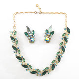 true vintage 1950s emerald green marquis rhinestones offset with smaller lighter green marquis cut rhinestone and smaller round aurora borealis blue rhinestones in a linked panel necklace wiht gold tone metal with matching clip on earrings in middle of necklace shown lying flat on white surface