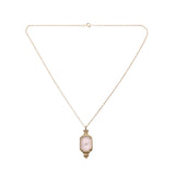 true vintage 1970s ice pink camphor glass with center rhinestone gold tone metal setting pendant on gold tone rope chain lying in inverted triangle on white background