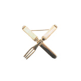 true vintage 1940s metal and mother of pearl handle fork and knife crossed in an x brooch shown lying flat on white background