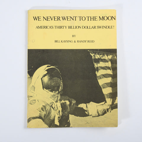 original 1976 1st edition book yellow soft cover We Never Went to the Moon America's Thirty Billion Dollar Swindle! by Bill Kaysing & Randy Reid with black lettering and picture of NASA astronaut with hand outstreched touching american flag at bottom of image shown in white background