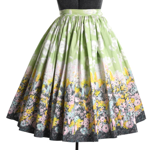 vintage 1960s green sky with clouds, floral, tree landscape border print full skirt shown on dress form against white background