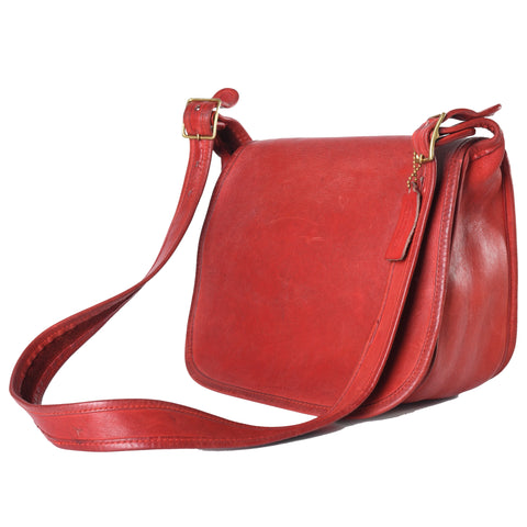 vintage 1970s red leather classic Coach pouch purse with strap resting in front of purse shown angled to left on white background