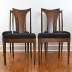 true vintage 1960s set of 4 brown walnut curved t back side dining chairs with black upholster shown with 2 chairs in front and two in back on hardwood floor and white background