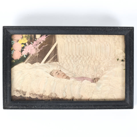 vintage 1940 black frame post mortem photography of elderly woman in casket with pink yellow flowers behind her