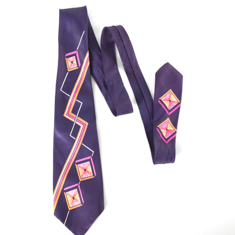 vintage 1950s blue necktie lying flat with 3 folds to show all patterns of neon pink, neon orange, white zig zags and geometric cubes