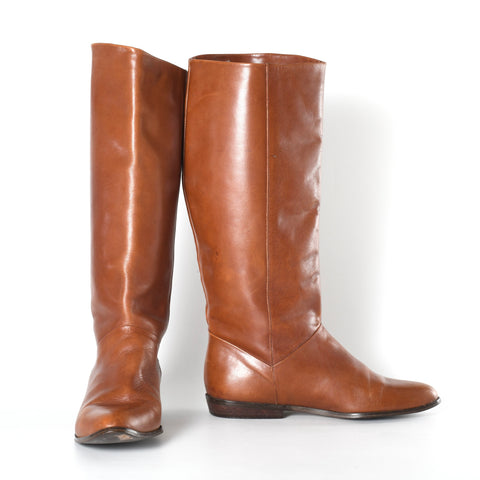 vintage 1980s tall brown leather boots with one on left facing forward and one on right of image facing to side showing small .75 inch heel
