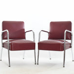 vintage 1940s maroon red Naugahyde bent chrome modern armchairs shown angled toward each other on a white background