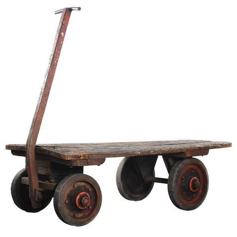 vintage wood top steel painted hand pull industrial 4 wheel dolly with orange paint wheels shown on white background at angle with handle on left of image